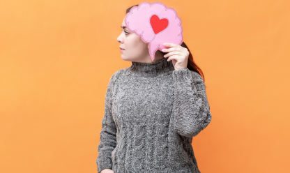 Picture of lady holding a brain picture with a heart in the middle up to her head