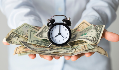 Hands holding pile of money and alarm clock